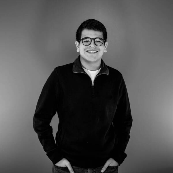 Marcelo Guzman Aguirre smiling, with glasses and a black shirt, hands in pockets, on a black and white background