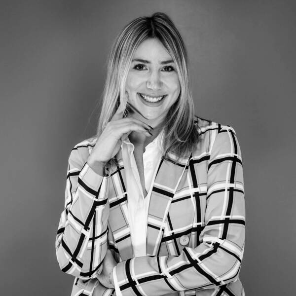 Holland Hiler smiling on black and white background, wearing a white blouse and checkered jacket
