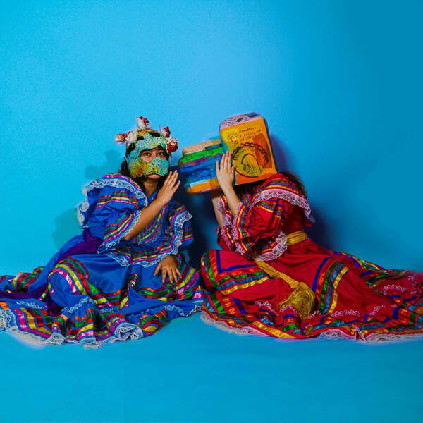 Blue background two women wearing masks whispering to each other