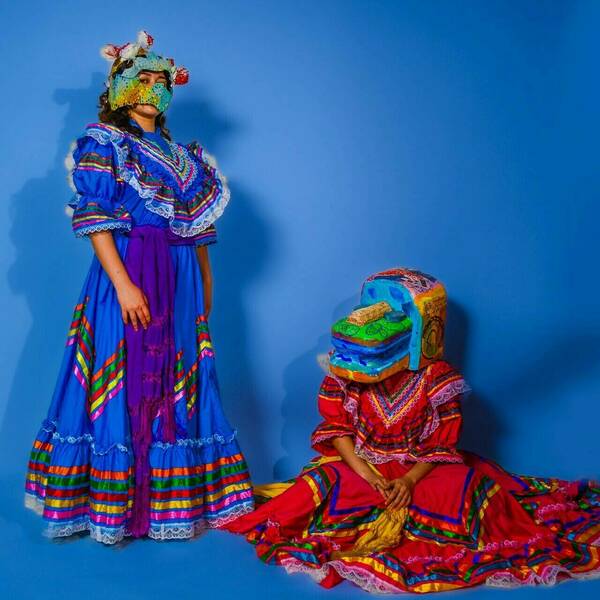 Two women wearing masks in front of a blue background, one in red, one in blue